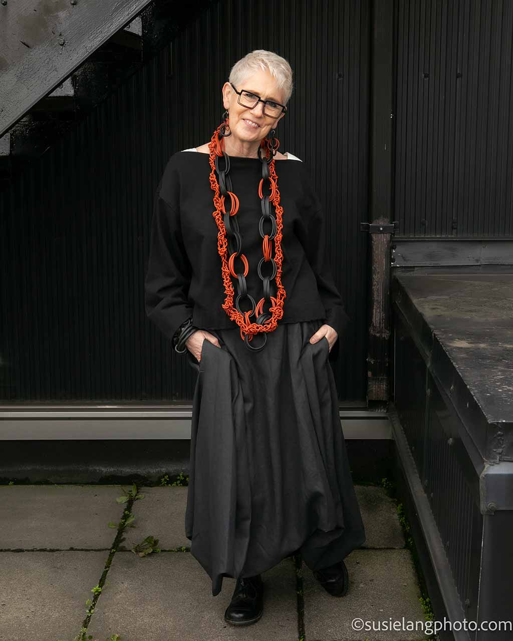 Rowan wearing black top and skirt and wearing recycled rubber necklace in black and tan and lightweight rubber earrings and bangles.