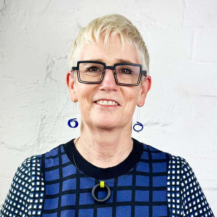 Woman in a blue and white top wearing glass and dangle earrings with blue swirl details