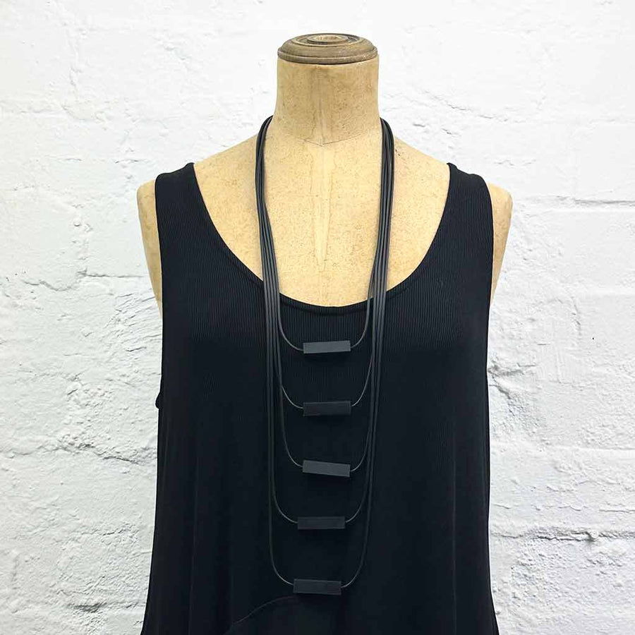 Long drop necklace with black small blocks displayed on a headless wooden mannequin