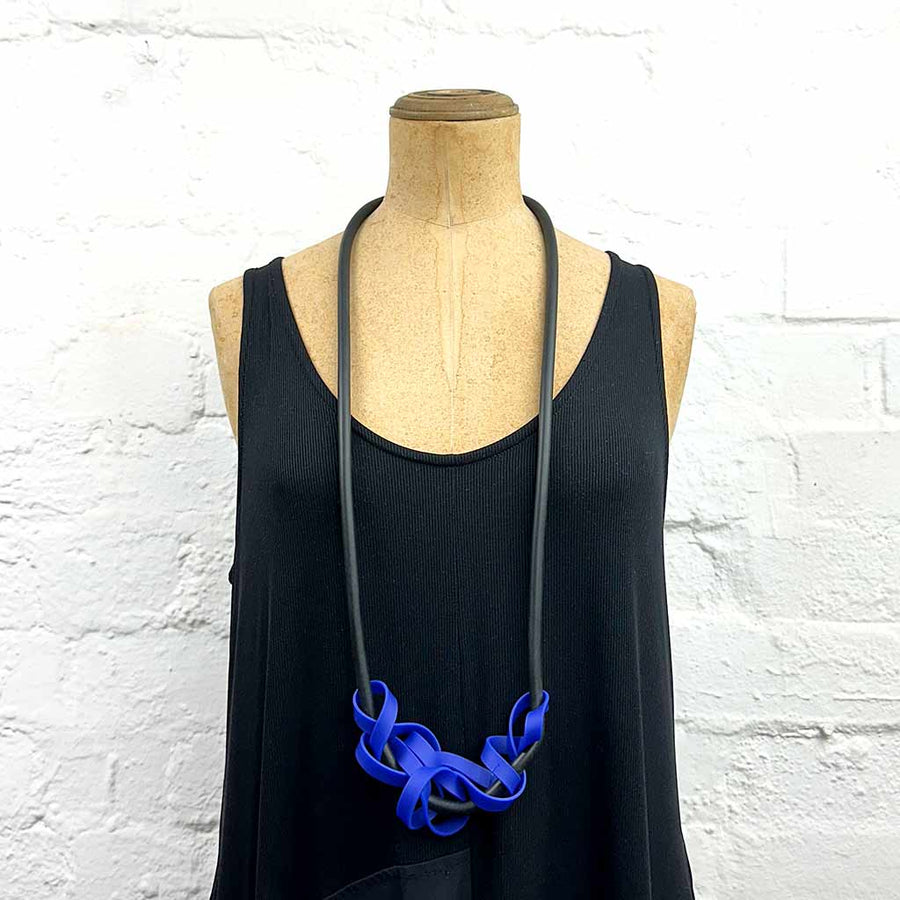 Mannequin displaying long necklace with tangled strips of blue rubber on black, soft rubber.