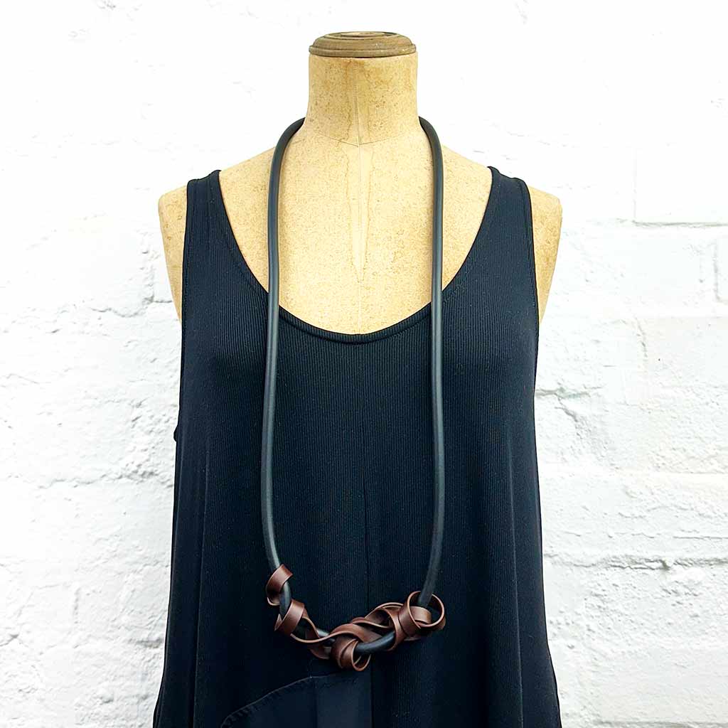 Mannequin displaying long necklace with tangled strips of brown rubber on black, soft rubber.