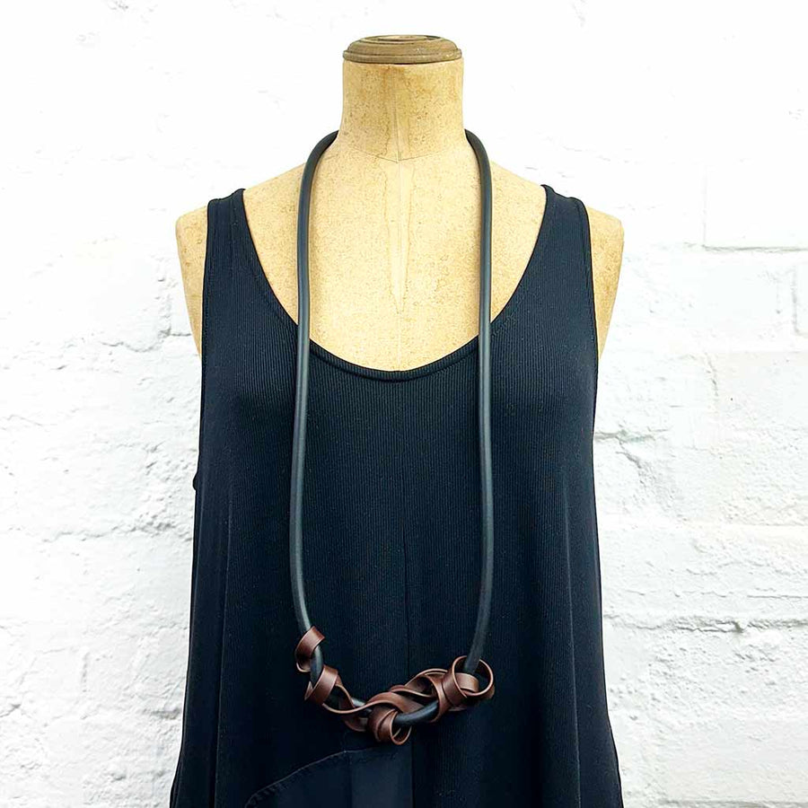 Mannequin displaying long necklace with tangled strips of brown rubber on black, soft rubber.