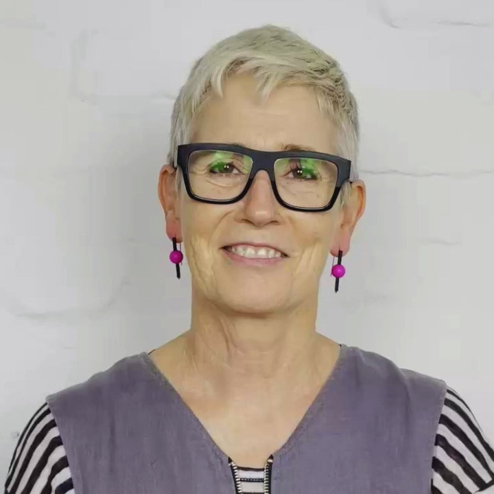 Video of woman wearing metallic bright pink spherical drop earrings with black vertical bars and hooked wire backs.