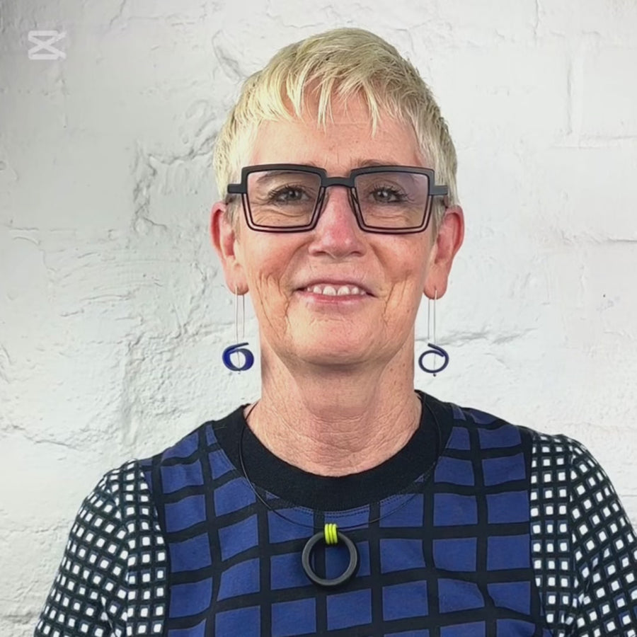 Video of woman wearing dangle earrings and rubber ring necklace