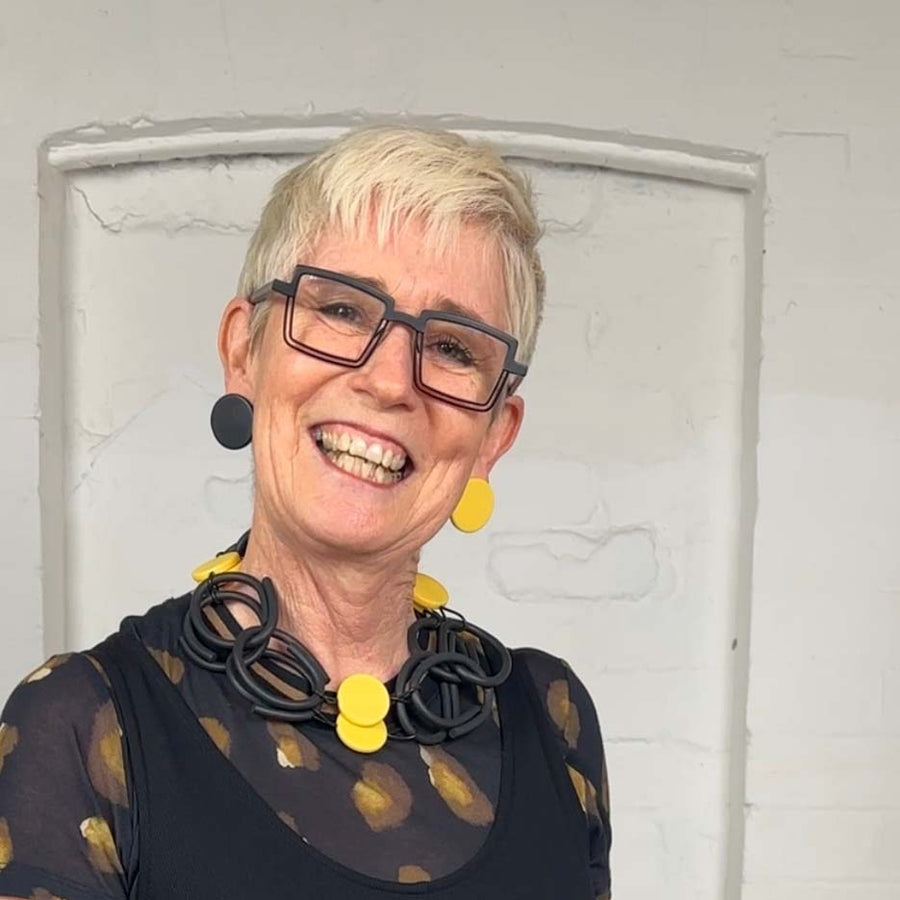 Close up of Rowan wearing yellow and black resin and rubber necklace and matching dot earrings.