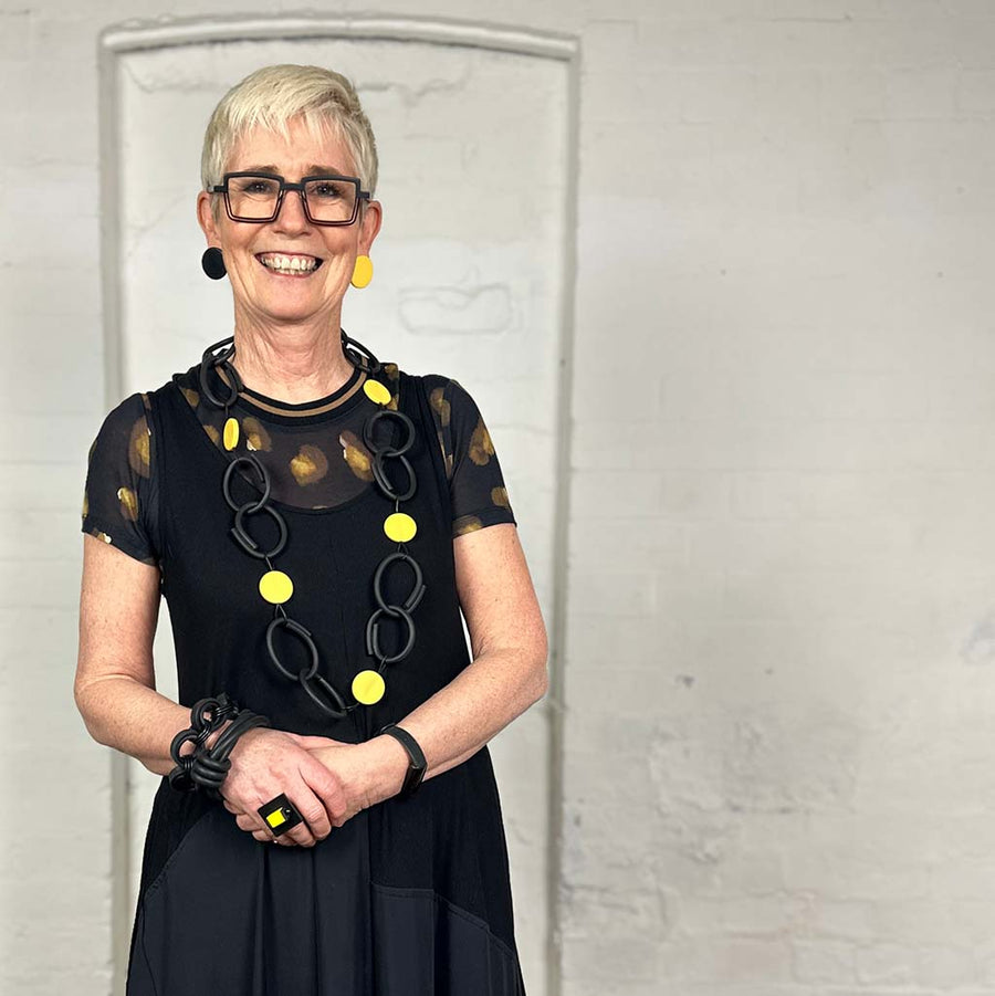 Rowan owner of Frank Ideas wearing a black dress. She is wearing yellow and black resin and rubber long chain necklace black with yellow dots.