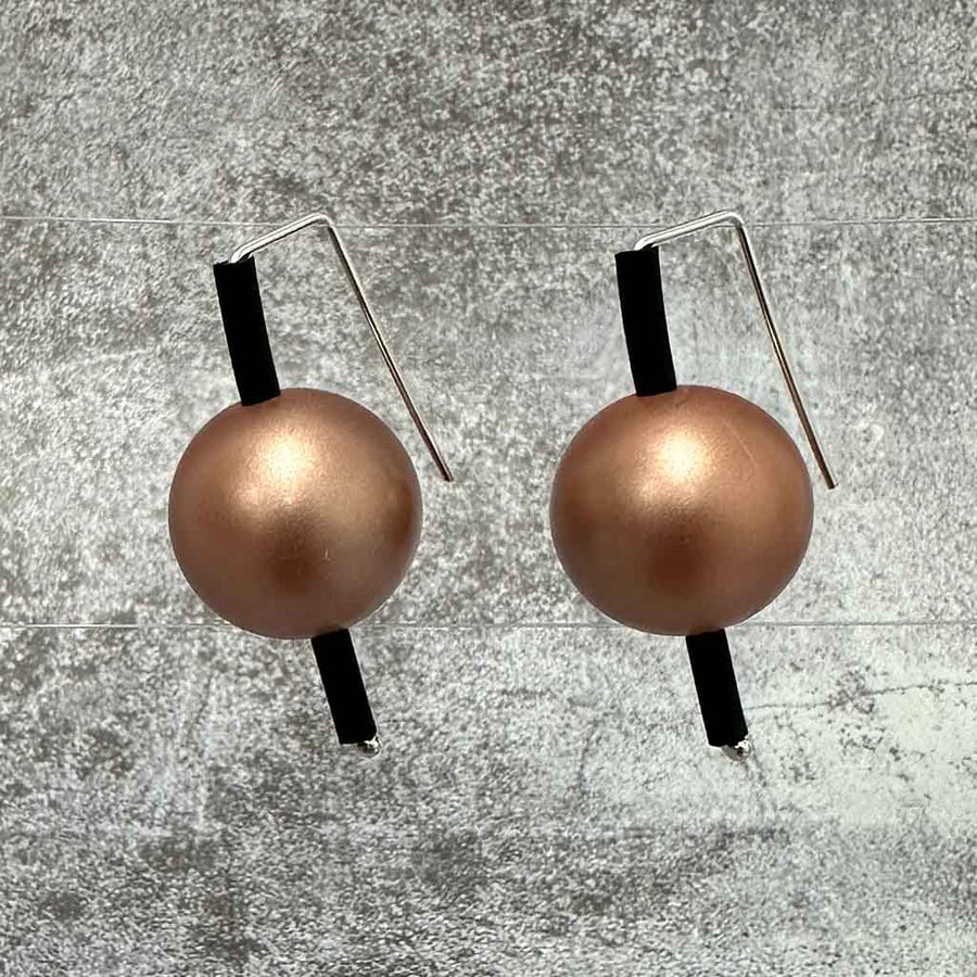 Two spherical earrings in metallic rose gold balls and vertical black bars on a concrete coloured background