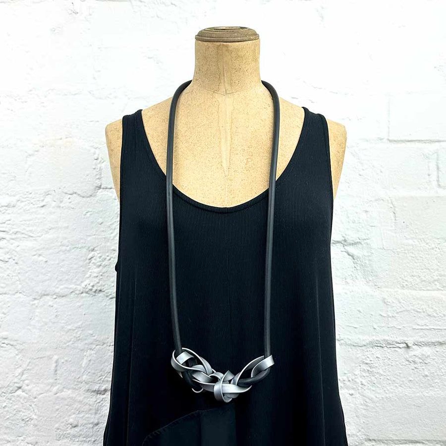 Mannequin displaying long necklace with tangled strips of grey rubber on black, soft rubber.