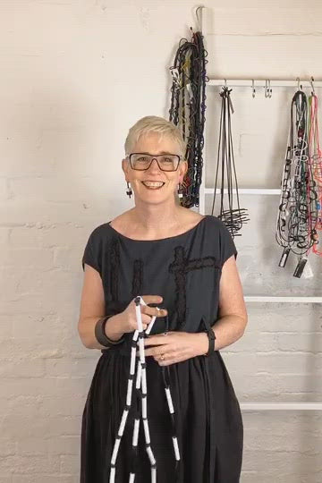 woman demonstrating how to wear black and white rod necklaces on a video