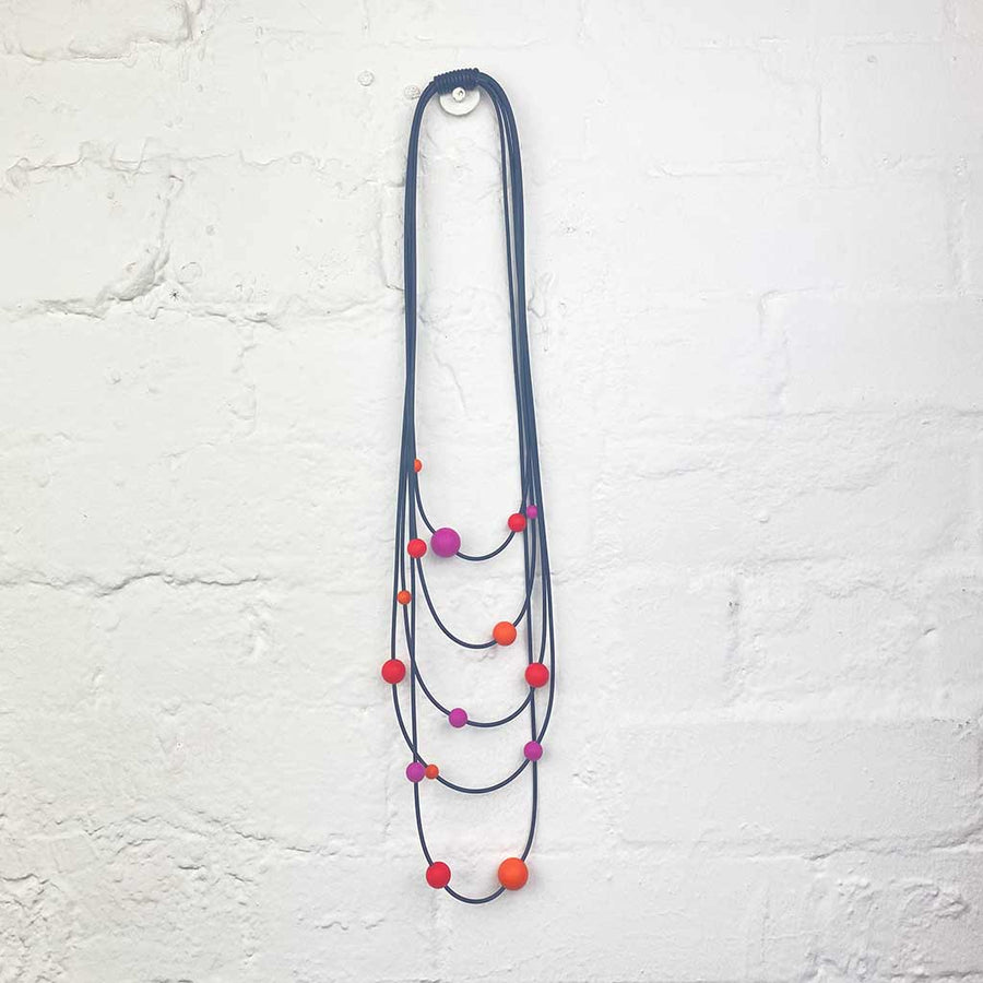 orange, pink and red long rubber necklace on a wall backdrop